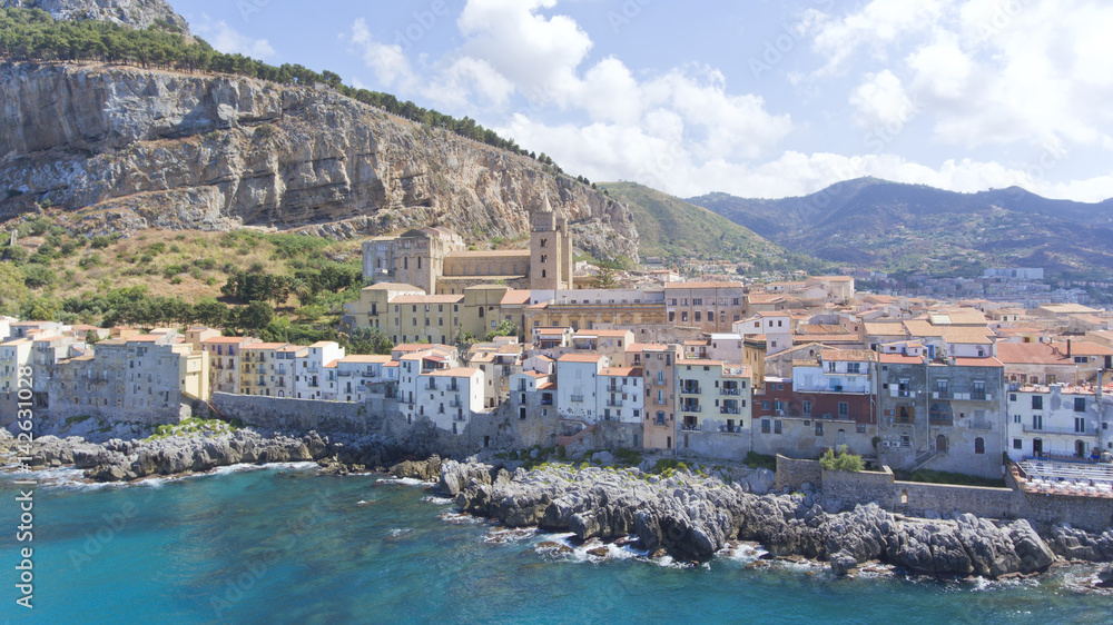Aerial view of a coastal Sicilian city of Cefalu, with historic houses on a rocky shore .