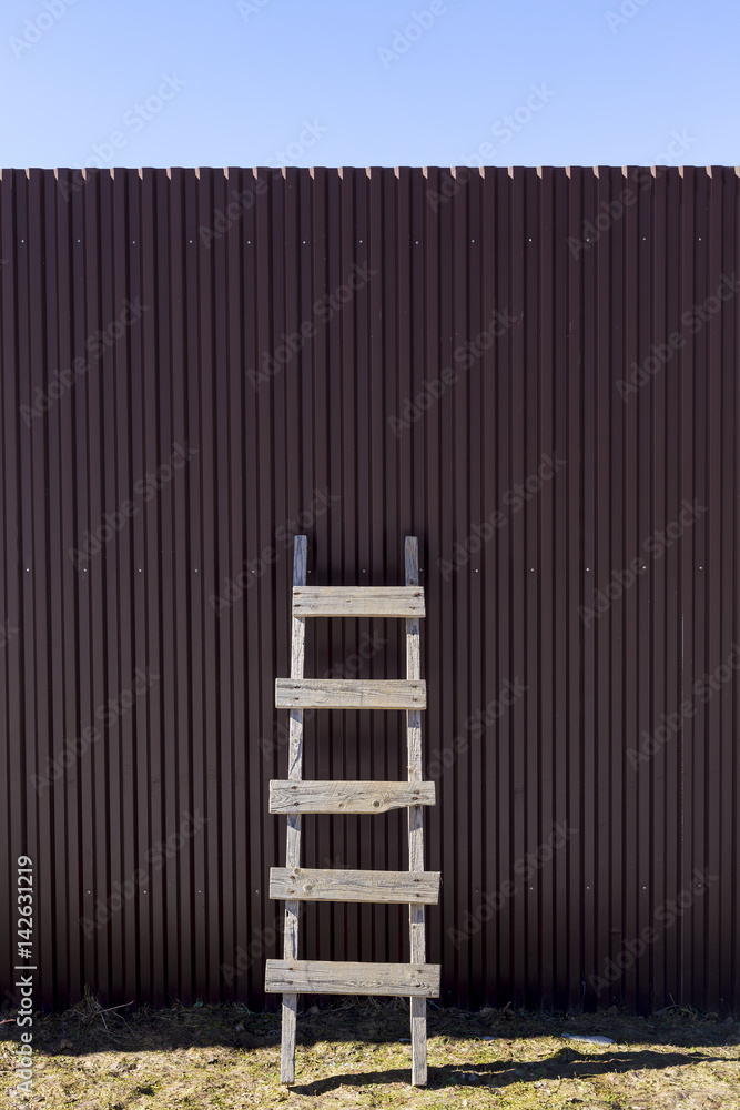 Home made wooden ladder standing at corrugated iron metal wall with blue sky background Home made wooden ladder standing at corrugated iron metal wall with blue sky background