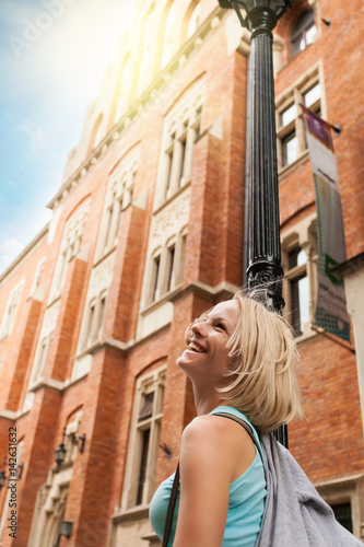 Young beautiful woman walking down the street along an old brick building against the background of sunlight. Building of the Collegium Mayus. Jagiellonian University in Krakow. Student life