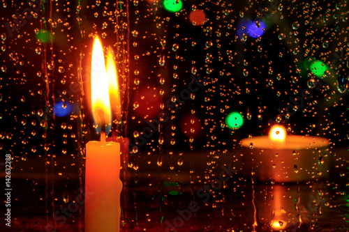 Candle stands in front of a window with rain drops.