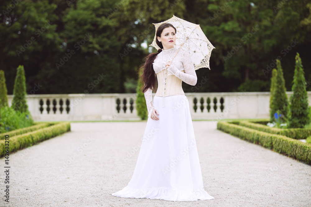 Woman in white Victorian dress with umbrella in park Woman in white Victorian dress with umbrella in park