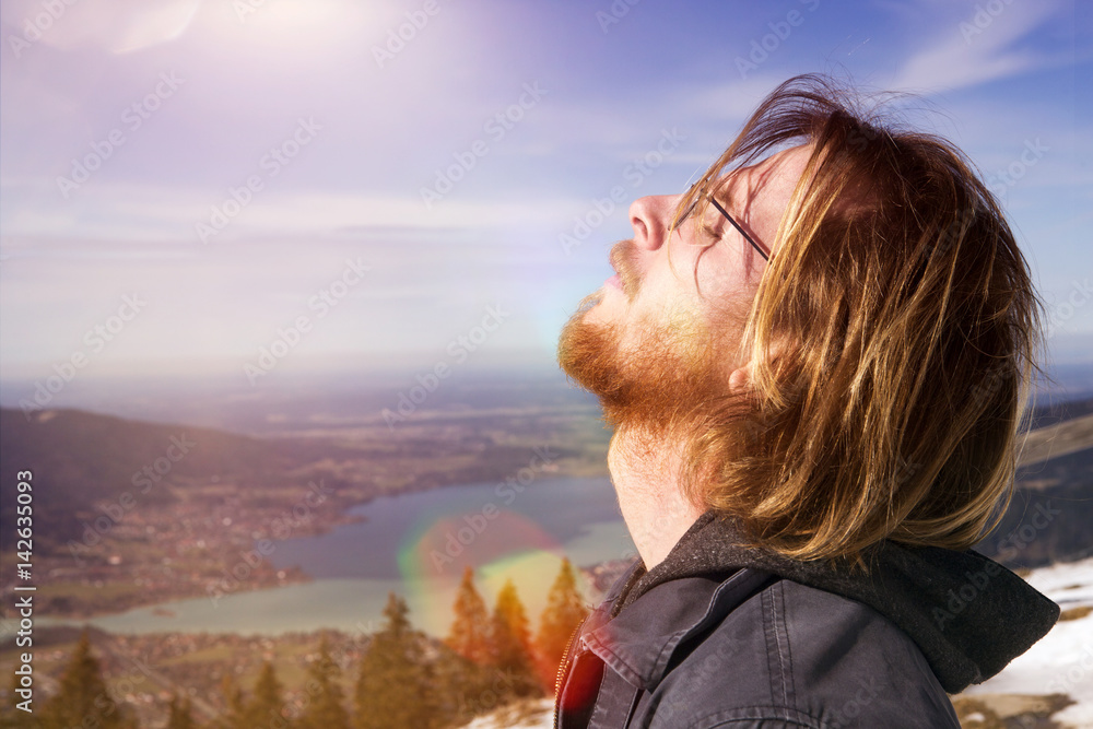 young man enjoying the sun with mountains and lake in the background young man enjoying the sun with mountains and lake in the background