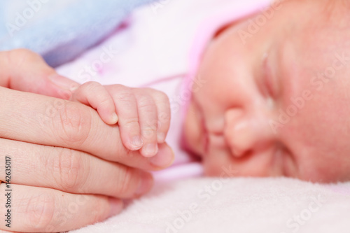 Baby sleeping in blanket holding mother hand
