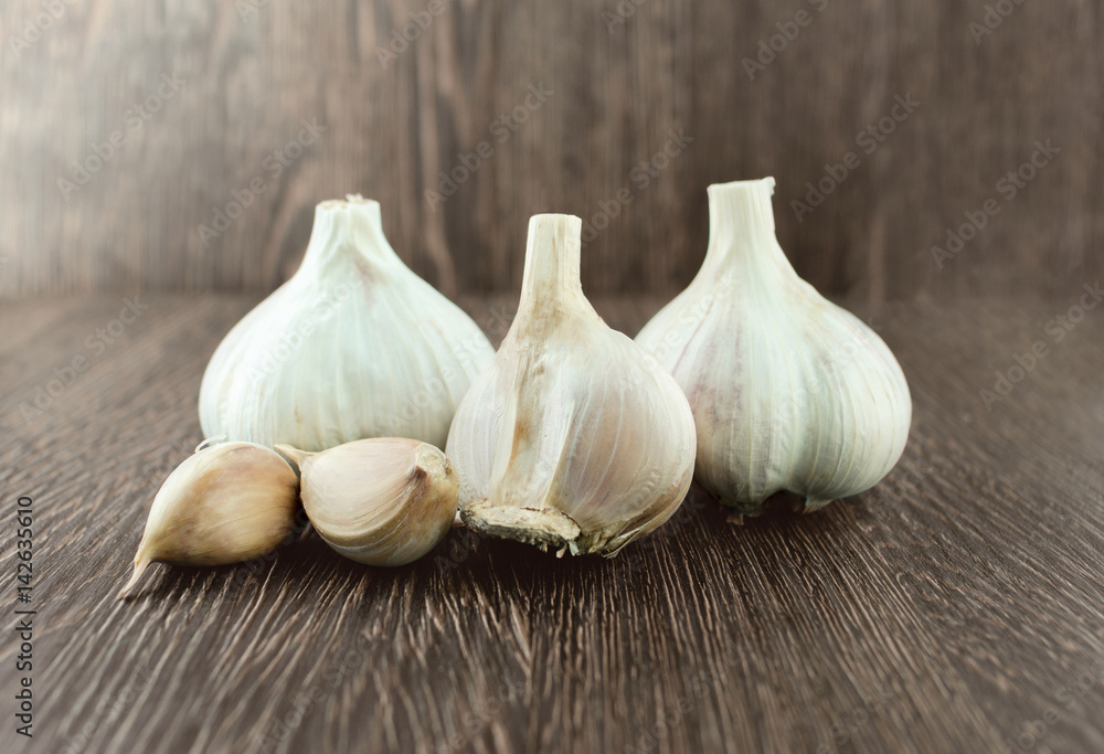 Obraz premium Garlic bulb and single cloveson wood background with shadow