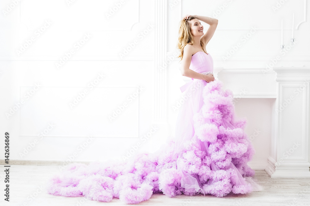 Dreamy woman portrait in a long pale purple ruffled gown in a white room. Elegant femininity Dreamy woman portrait in a long pale purple ruffled gown in a white room. Elegant femininity