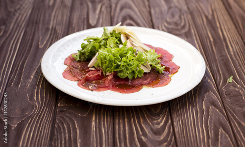Carpaccio served with lettuce and parmesan in white plate in restaurant. Close-up view