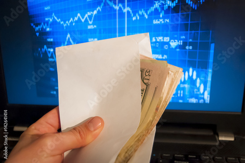 фотографія Hand holding envelope with money, stock exchange graph on the background