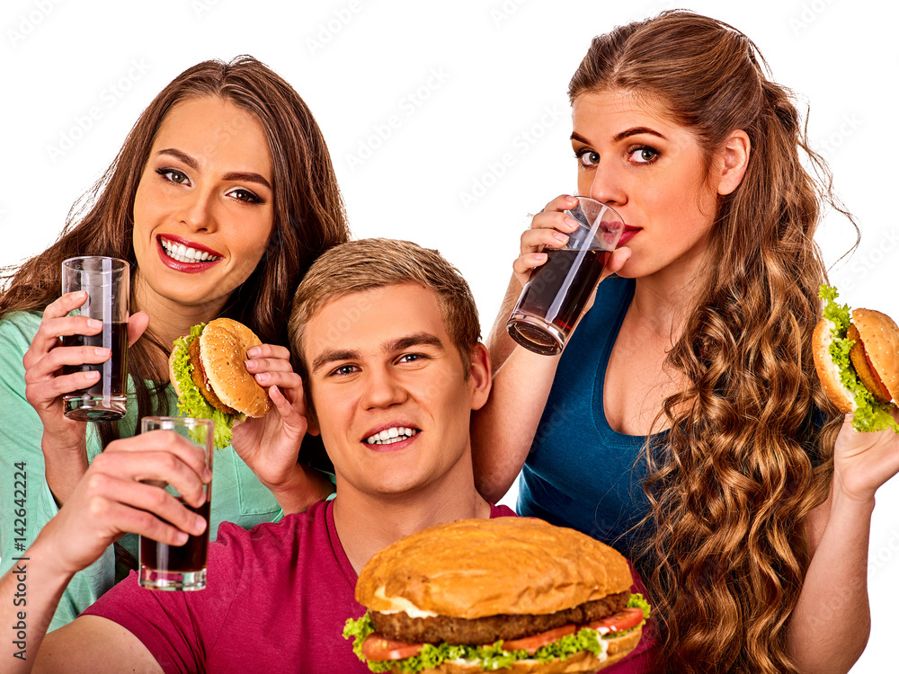 Hamburger fast food with ham in people hands . Fast food concept. Man and two women drink glass cola on eating party. Girls fool around and feed man.