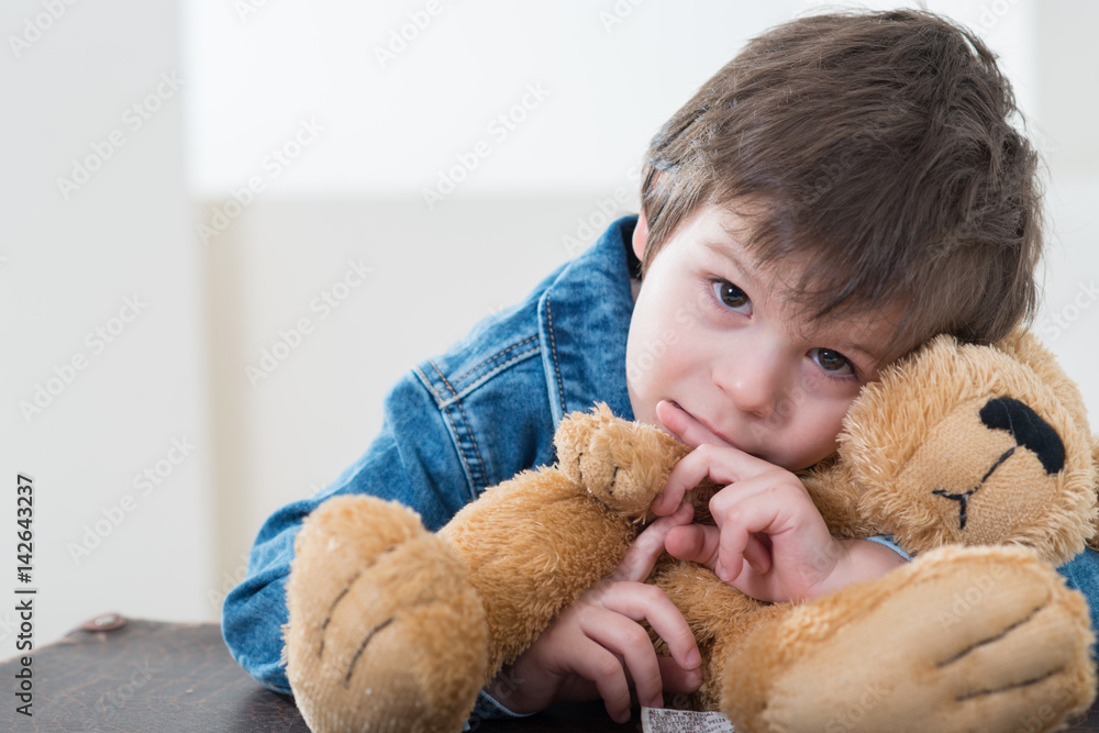 Little boy sitting on the travel retro brown suitcases in jeans jacket trully hugging a bear Little boy sitting on the travel retro brown suitcases in jeans jacket trully hugging a bear