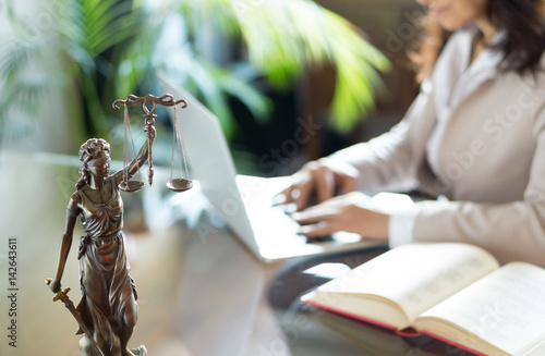 Statue of Justice and lawyer working on a laptop. Selective focus.
