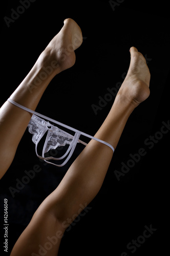 Low key photo of sexy female legs in fetish g-string cutout thong against dark background