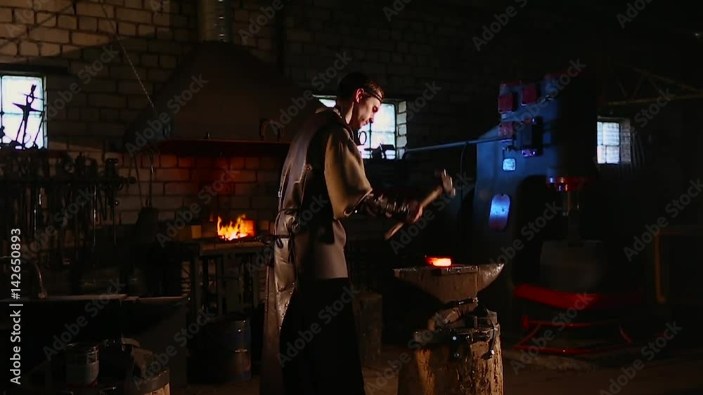 The blacksmith manually forging the hot metal on the anvil in smithy with spark fireworks. The blacksmith manually forging the hot metal on the anvil in smithy with spark fireworks.