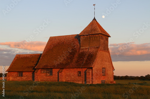 Summer sunset at St Thomas a Becket Church, Fairfield, Romney Marsh with the moon rising high in the sky above the church