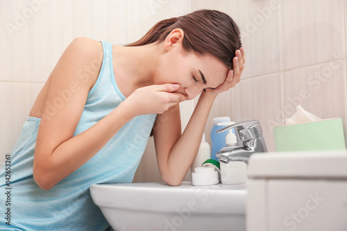 Young vomiting woman near sink in bathroom