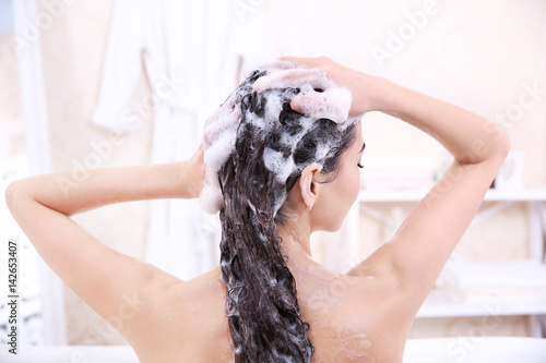 Beautiful young woman washing hair in bathroom at home