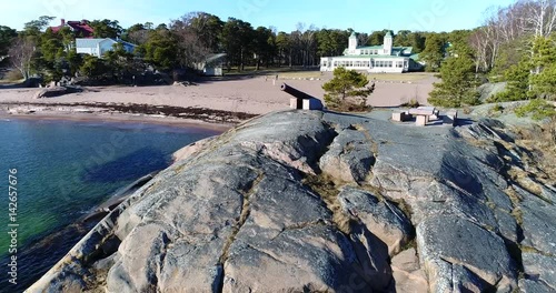 Hanko Casino, Cinema 4k aerial rising view behind a cliff with a old cannon, rewealing the casino, on a sunny spring day, in Hango, Finland