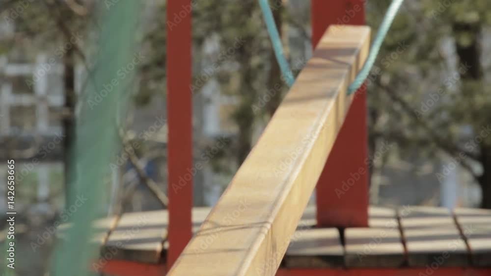 Young female climber walks by pendant log bridge on high ropes course in extreme park Young female climber walks by pendant log bridge on high ropes course in extreme park