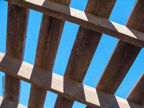Blue sky as seen through weathered top of wooden pergola