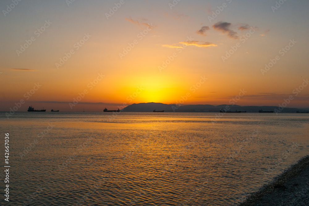 Natural summer sea sunset. Silhouettes of ships and strip of land on the horizon. Orange sea sunset in evening