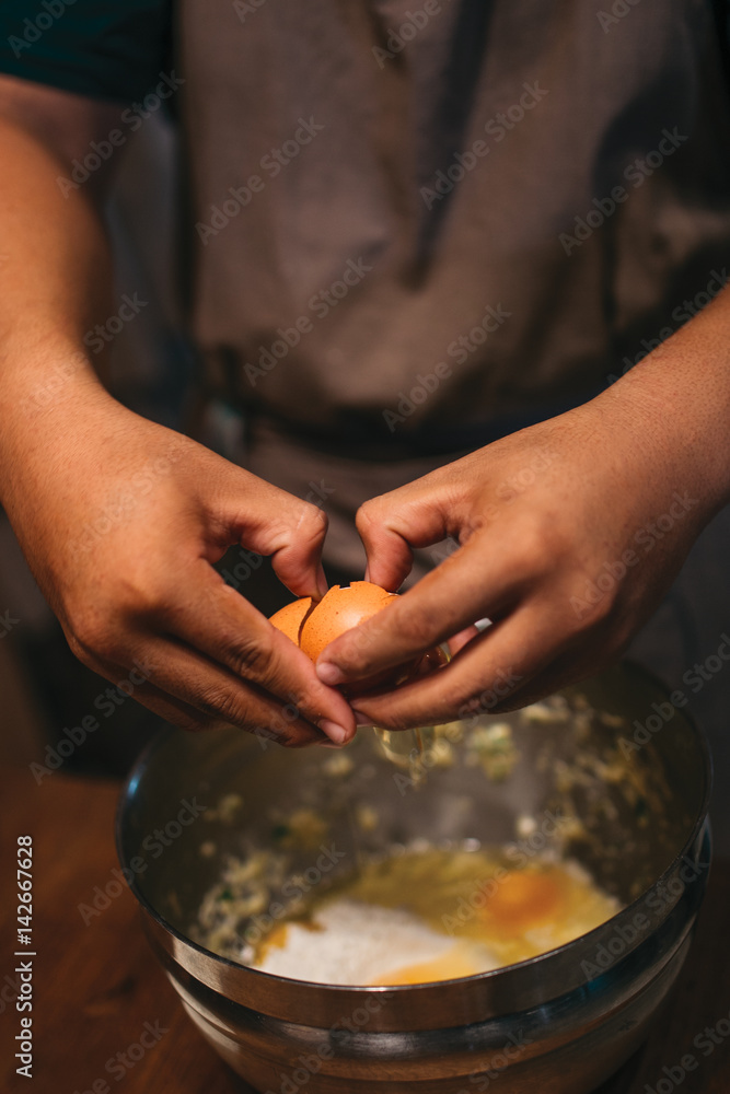 Close up of hands with egg under the metal bowl, making a adough on the wooden table