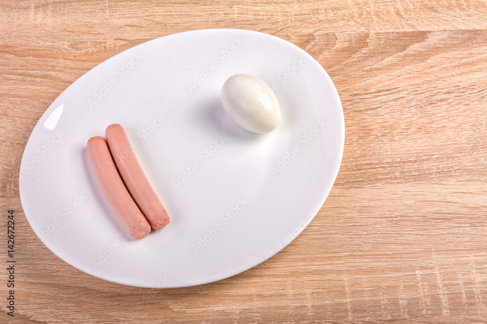 Two frankfurter sausages and egg on white plate on kitchen table.Close up shoot and top of view Two frankfurter sausages and egg on white plate on kitchen table.Close up shoot and top of view