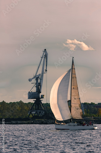 Sailboat moving past the cargo crane in evening, Latvia © InfinitumProdux