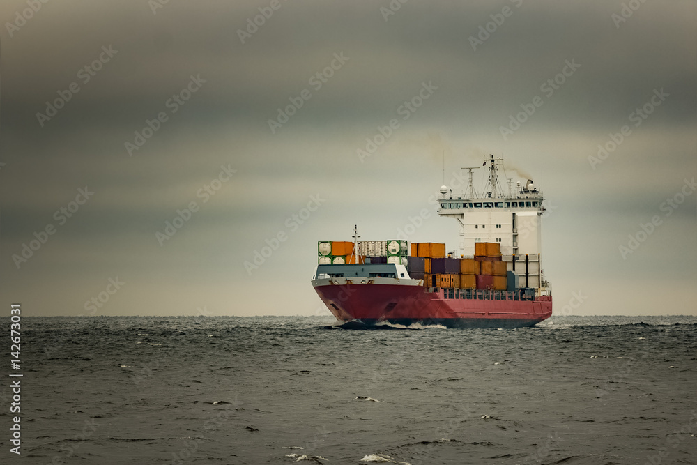 Red cargo container ship sailing from Baltic sea in cloudy day Red cargo container ship sailing from Baltic sea in cloudy day