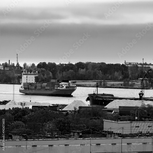 Red container ship entering port of Riga, Latvia. Monochrome