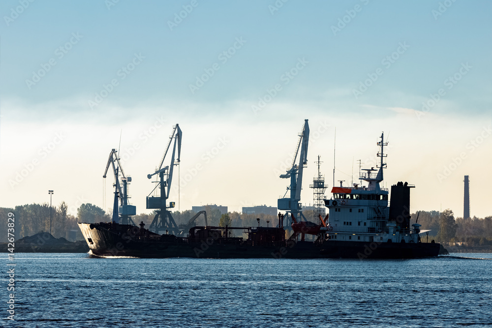 Black cargo oil tanker moving past the cargo cranes
