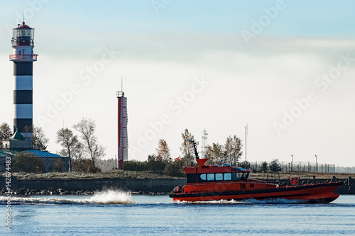 Red pilot ship sailing past the lighthouse in Riga