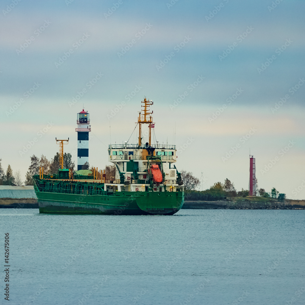 Naklejka premium Green cargo ship moving to the port in cloudy day