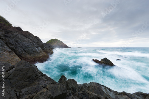 A rough, luminous blue ocean washes around a rocky headland under a stormy sky in this beautiful seascape.