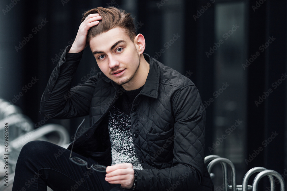 Fashionable man sitting near the wall with glasses on hands Fashionable man sitting near the wall with glasses on hands