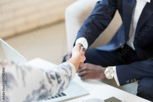 Happy businesswoman handshaking with client closing deal in an office interior with a window in the background