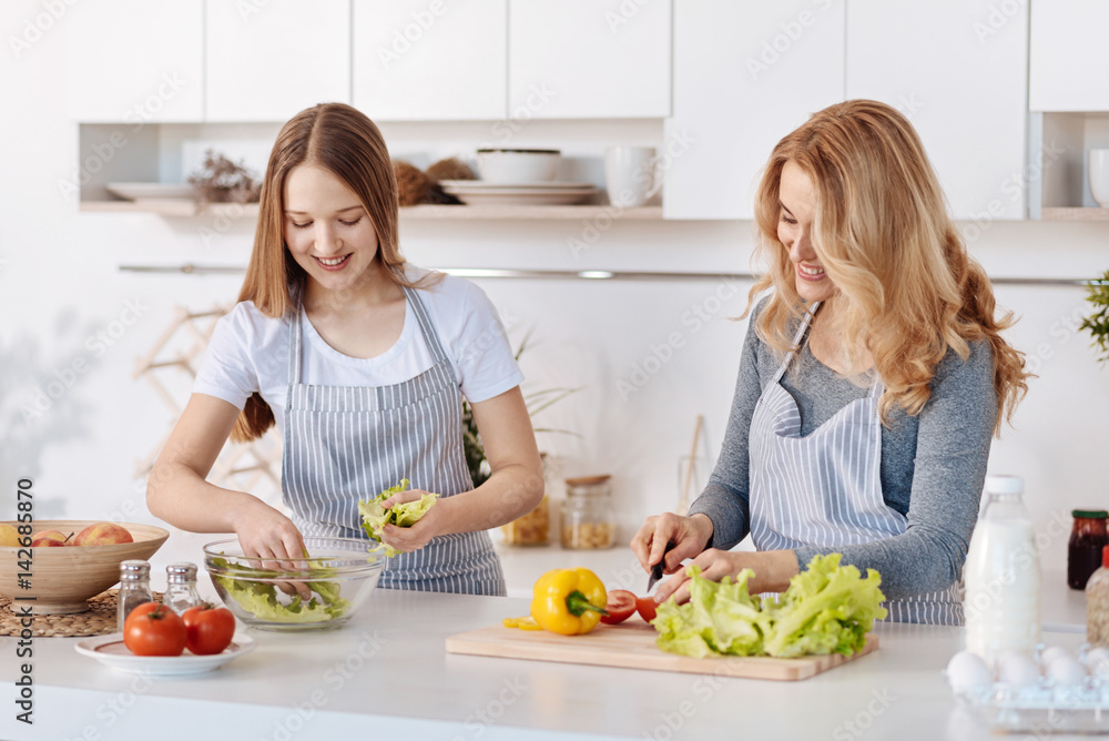 Pleasant mother and her teenage daughter cooking vegetable salad