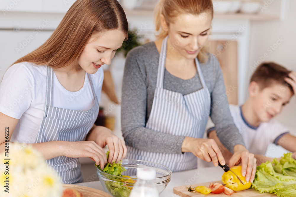 Pleasant loving mother cooking salad with her children