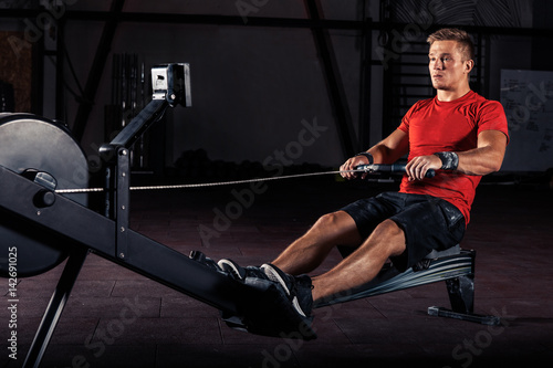 Obraz na płótnie young man using rowing machine in the gym w salonie