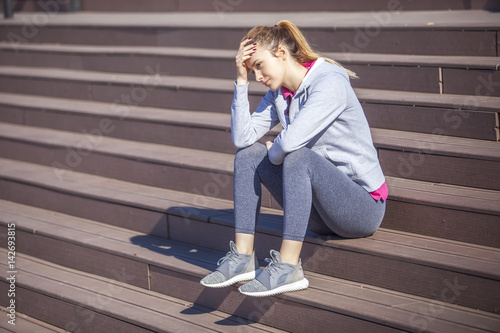 Young woman with abdominal pain after sitting on the steps of recreational running