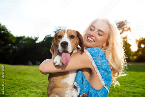 Young beautiful blonde girl walking, playing with beagle dog in park. © Cookie Studio