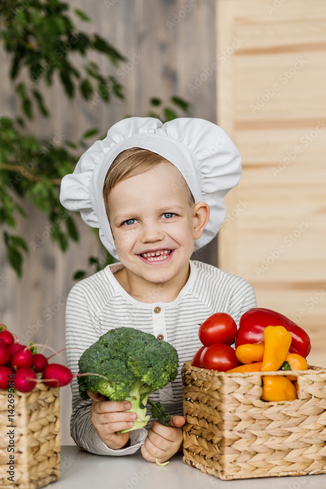 Handsome little kid in chef uniform with vegetables. Cooking in kitchen at home. Vegetarian. Healthy food Handsome little kid in chef uniform with vegetables. Cooking in kitchen at home. Vegetarian. Healthy food