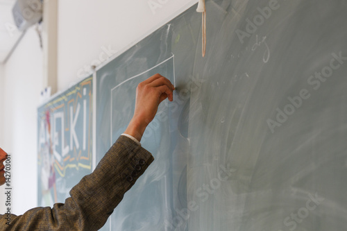 The hand of a teacher in a classroom with a chalk board.