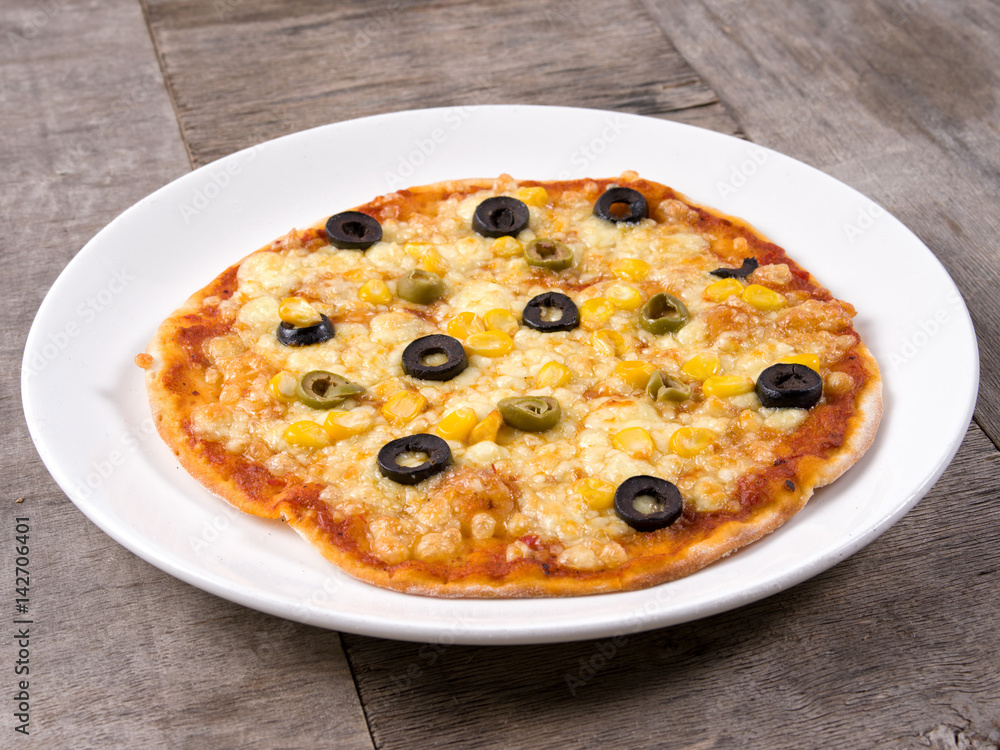 Cheesy Pizza topped with corn and olives served in a white plate on wooden background