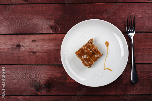a piece of chocolate brownie and caramel sauce on a white plate. Top view