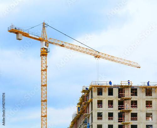 Crane and workers at construction of residental building.