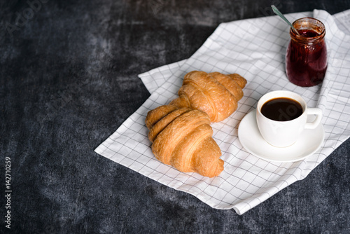 Picture of croissants, pot with jam and coffee cup aside on grey table