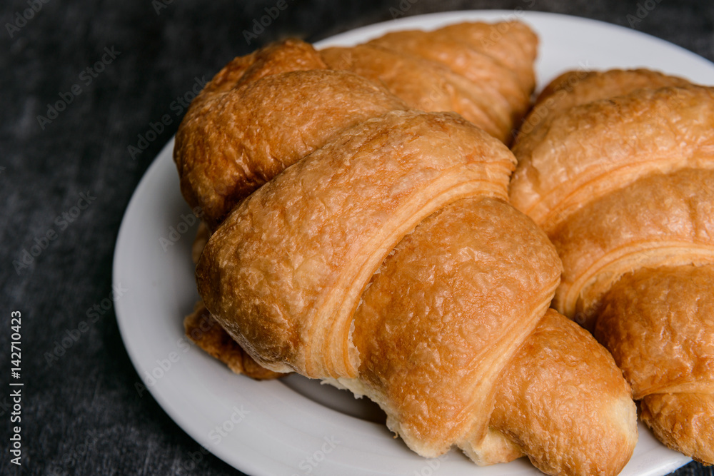 Macro picture of croissants on white round plate and grey table background. 