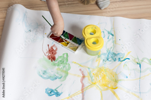 The kid draws a line with watercolor paints on white paper