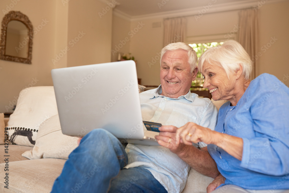 Happy seniors shopping online from their living room sofa