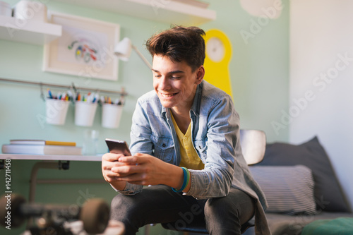 Teenage boy texting message in his room photo