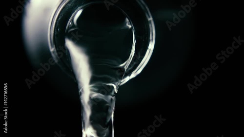 Clean water pours from the bottleneck of a glass bottle, close-up, black background, slow mo